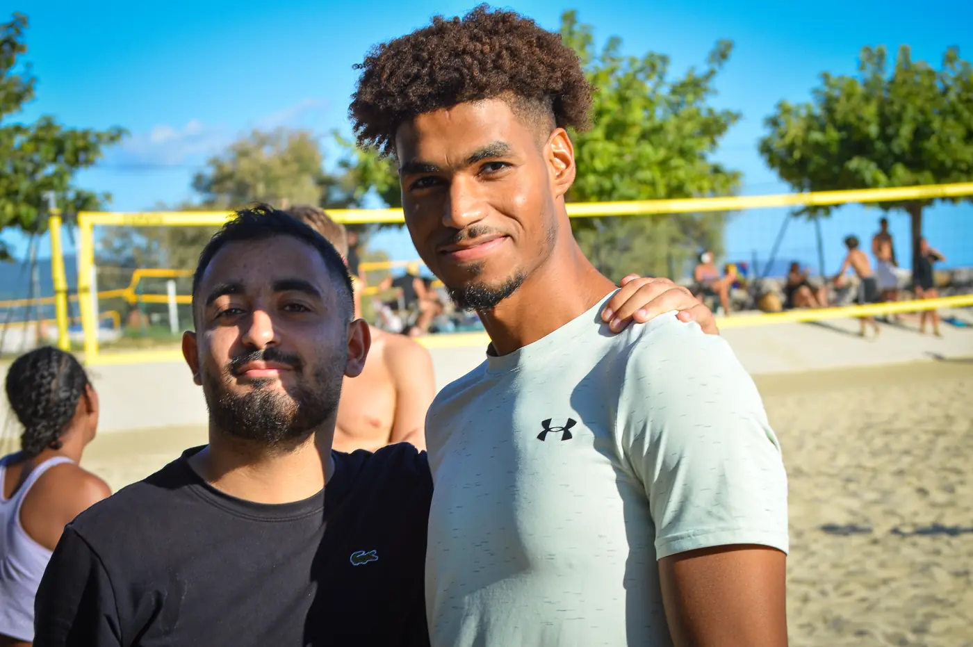 Deux membres du Mourillon Volley souriants devant les terrains de beach volley de la plage du Mourillon, à Toulon