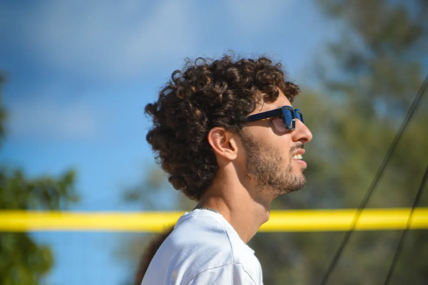Un joueur du Mourillon Volley de profil devant le filet jaune d'un terrain de beach volley, ciel bleu en arrière-plan